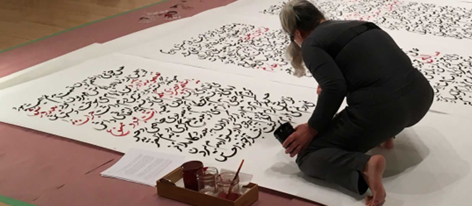 A young woman works on a huge piece of art - a set of Arabic texts painted by hand onto very large pieces of paper.