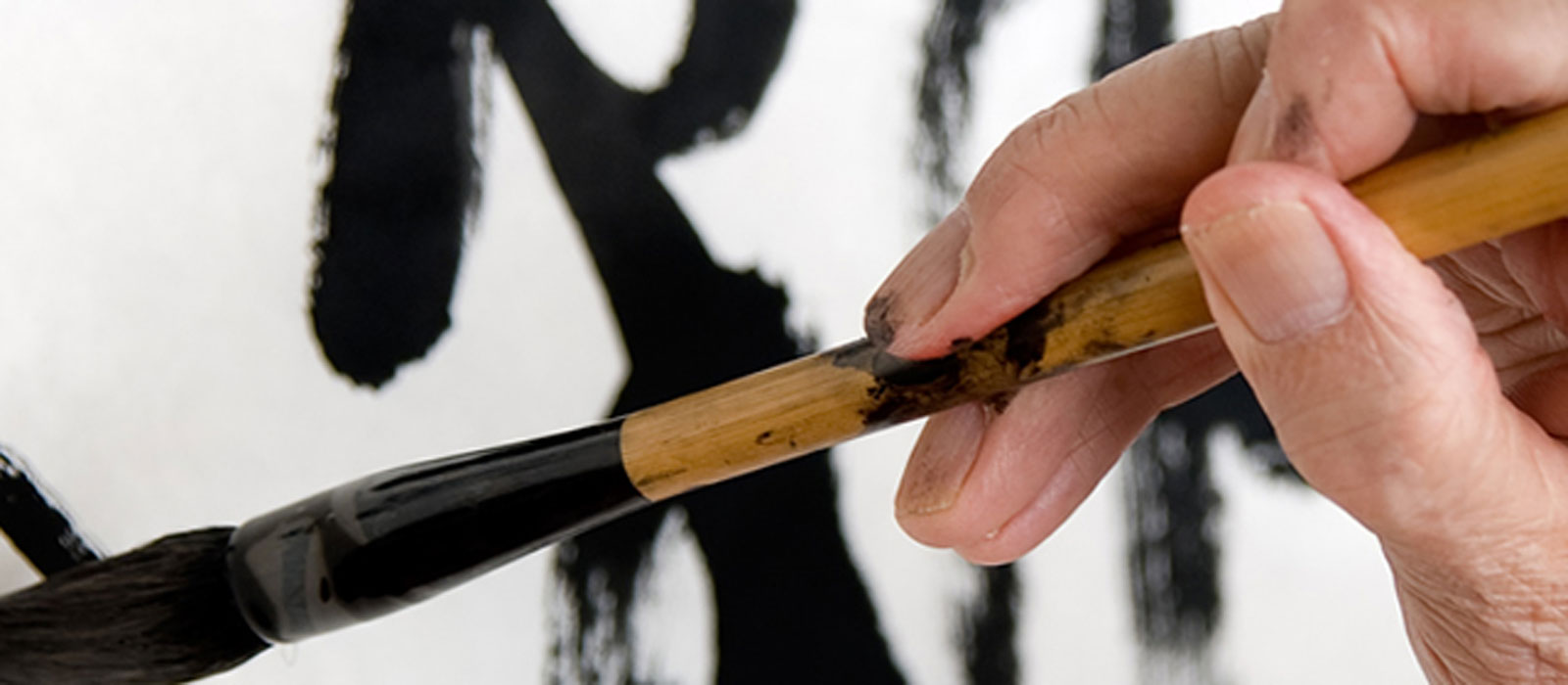 An older person uses a Chinese calligraphy brush to render very large characters from an Asian language onto big sheets of paper.